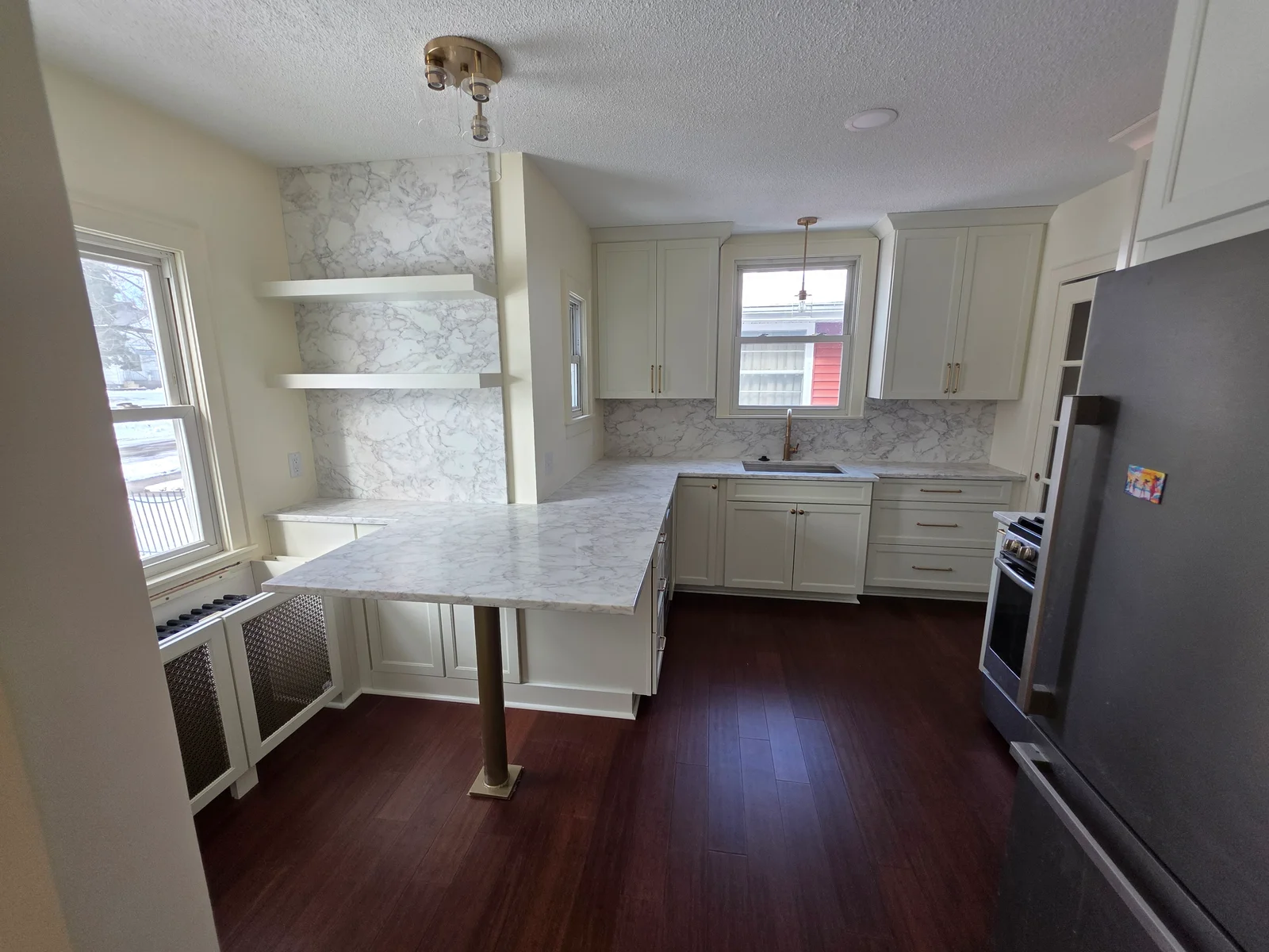 Kitchen with white shaker cabinets, marble-look countertops, floating shelves, and dark wood-look flooring
