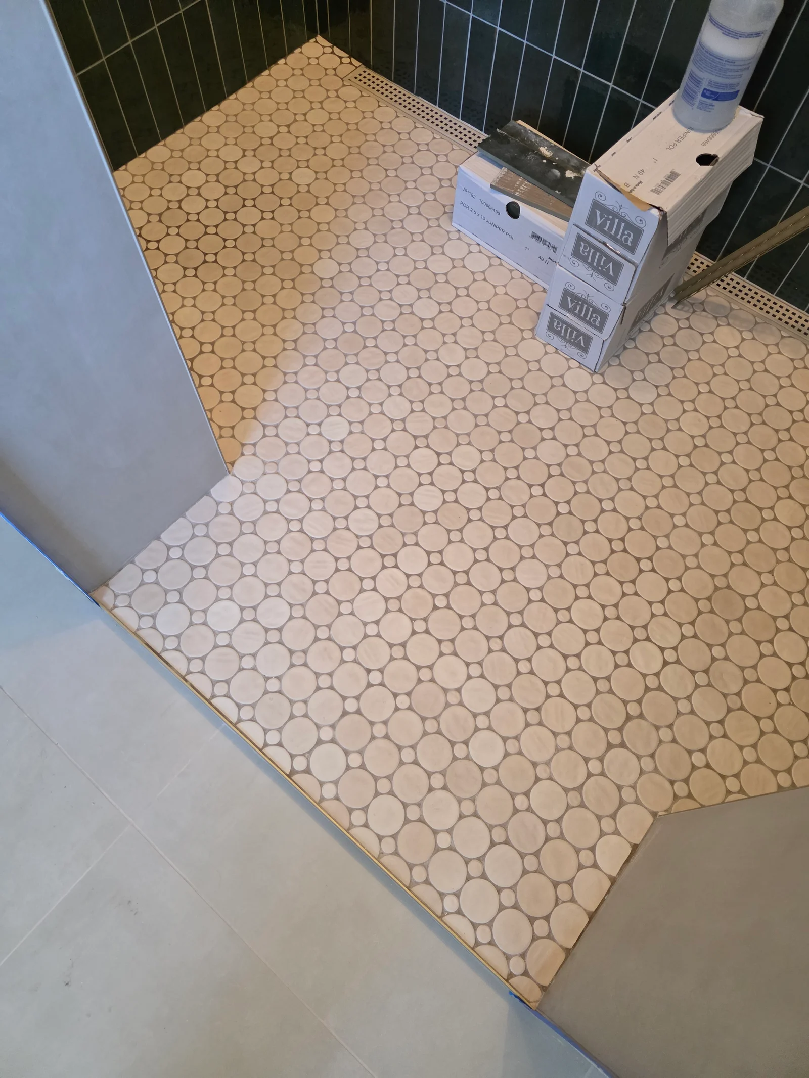 Cream penny round mosaic tile shower floor with brass trim, dark green subway tile walls, and linear drain