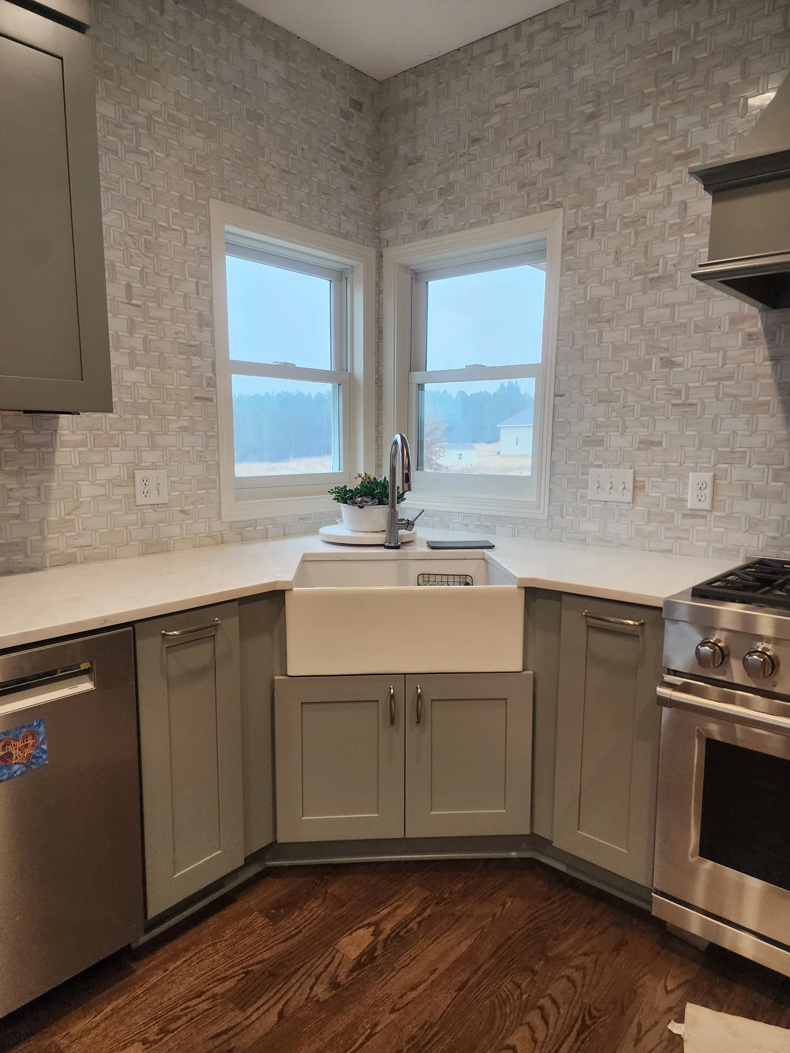 Sage green shaker cabinets, white quartz countertop, farmhouse sink, and woven mosaic tile backsplash in corner kitchen