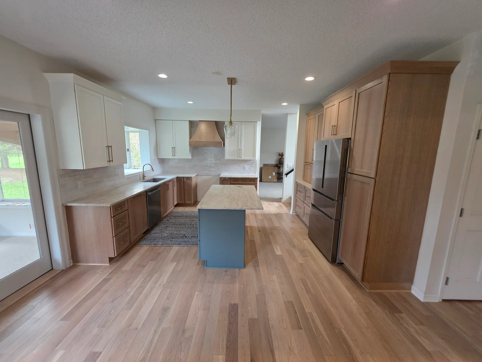 Kitchen with white shaker cabinets, natural wood cabinets, blue island, stone countertops, wood range hood, and light oak hardwood floors