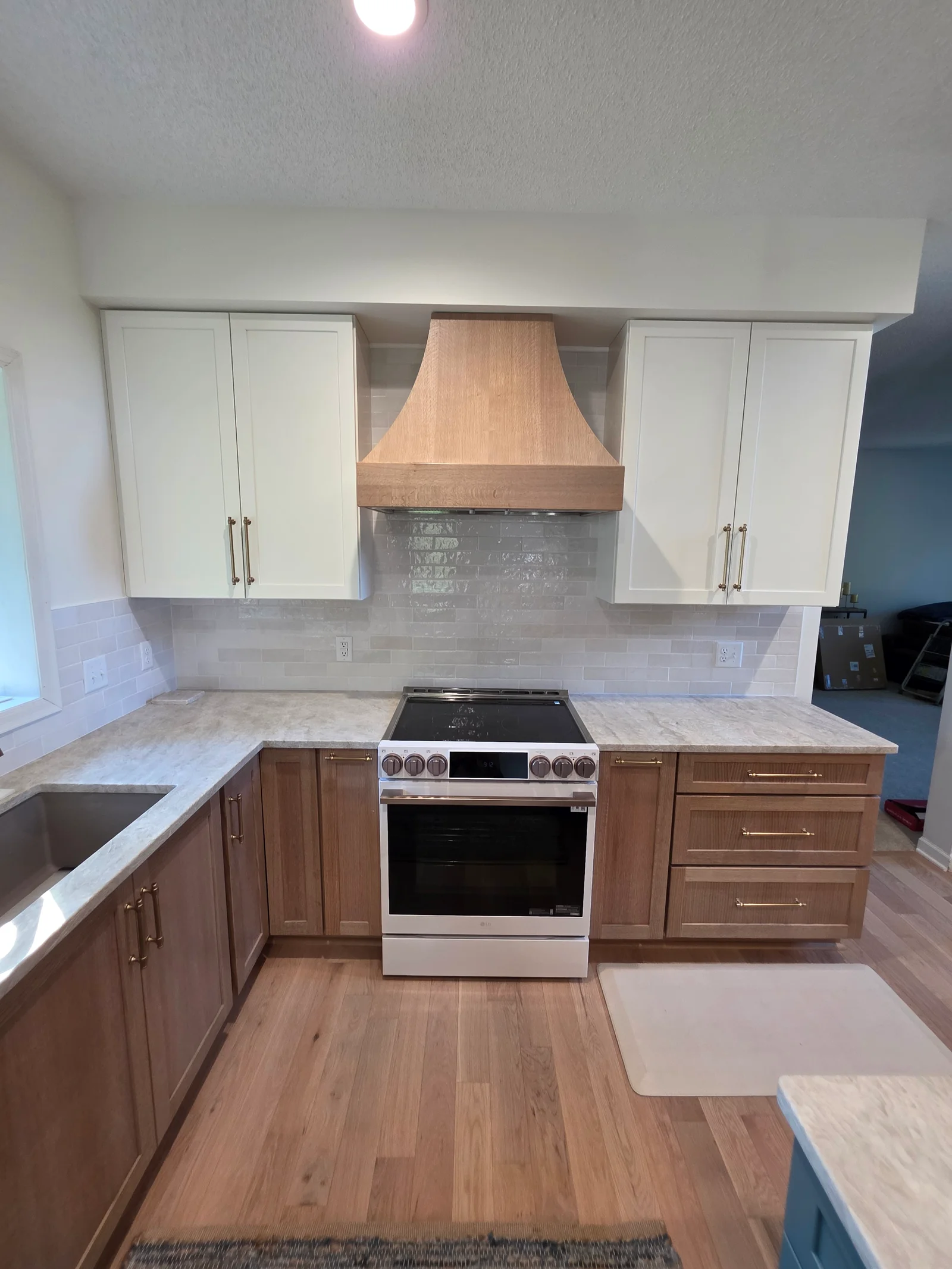 Kitchen with white shaker cabinets, wood lower cabinets, curved wood range hood, gray subway tile backsplash, and light stone countertops