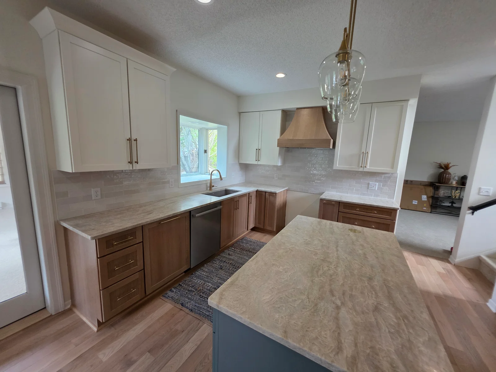 Kitchen with white shaker upper cabinets, natural wood lower cabinets, wood range hood, veined countertops, and teal island