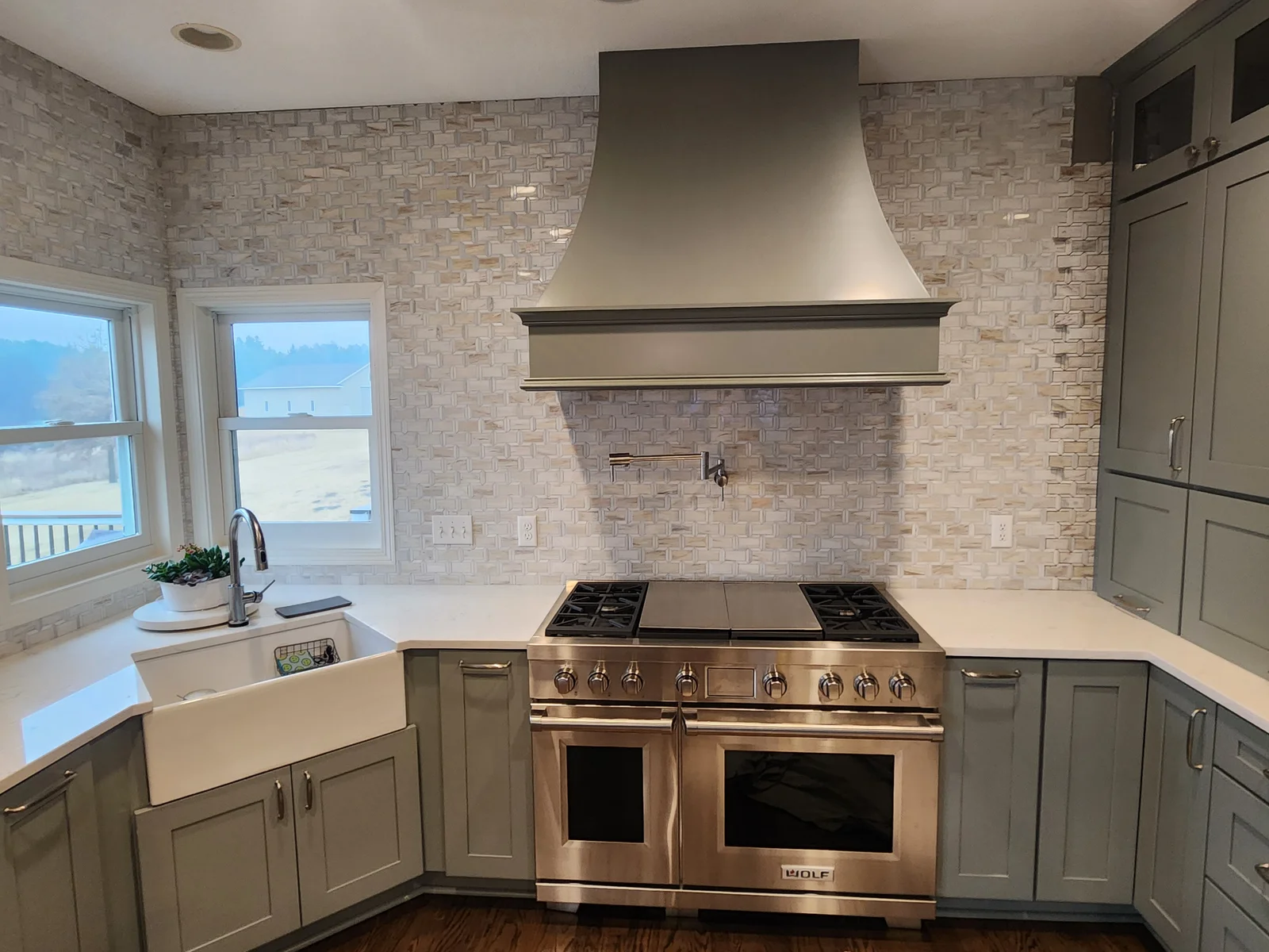 Kitchen with sage green shaker cabinets, white quartz counters, farmhouse sink, Wolf range, custom hood, and mosaic tile backsplash
