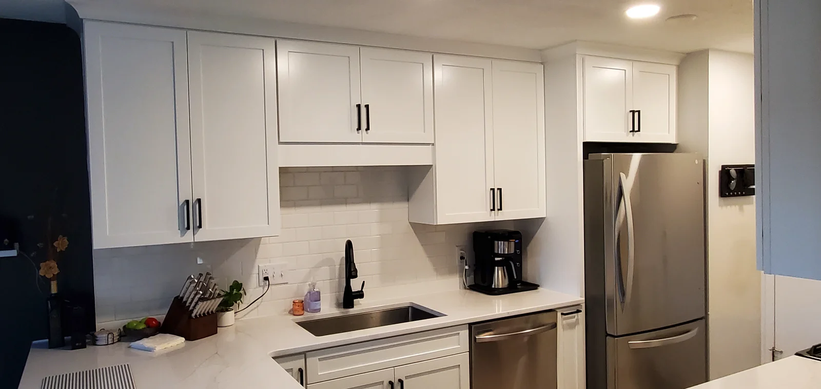 White shaker cabinets with black pulls, quartz countertops, subway tile backsplash, and stainless steel sink in kitchen