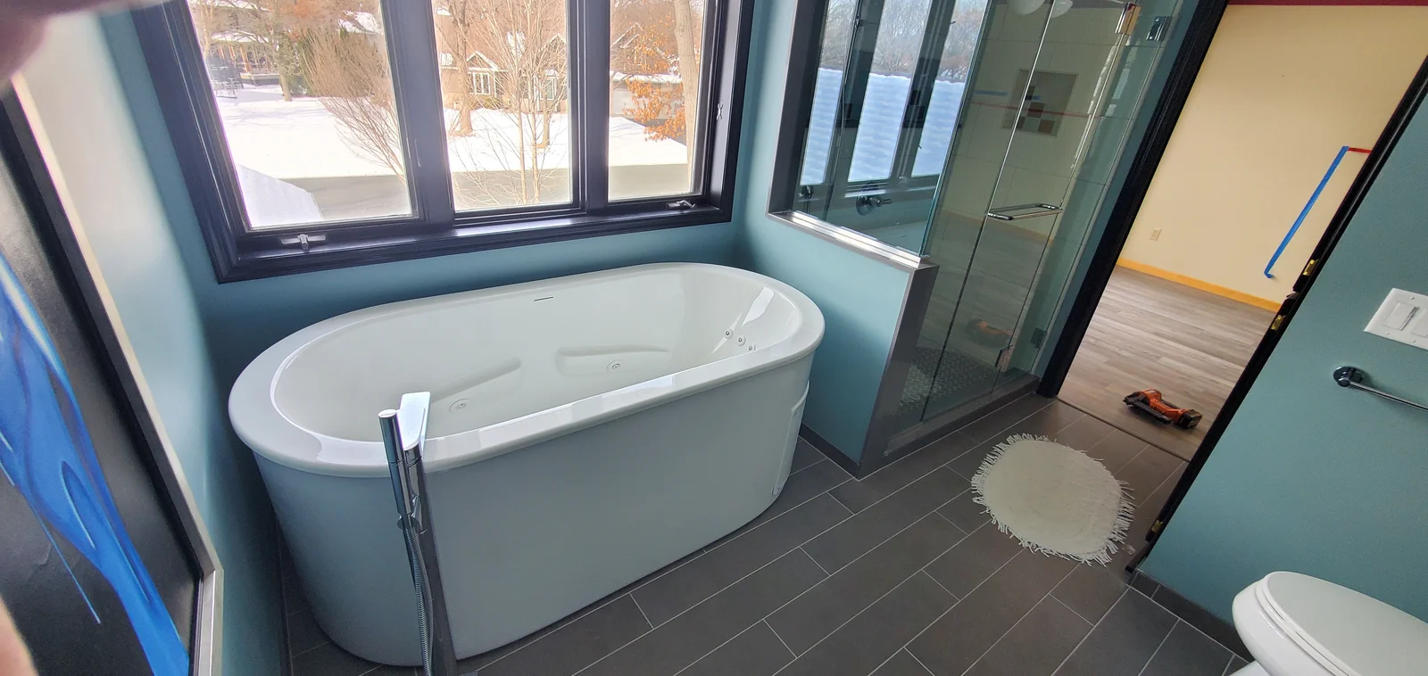 Freestanding oval soaking tub with chrome floor filler beside a frameless glass shower and dark gray porcelain tile floor